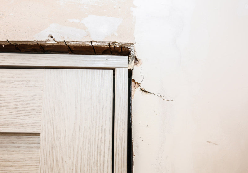 Gap between an external door frame and wall with visible cracks and unfinished plasterwork